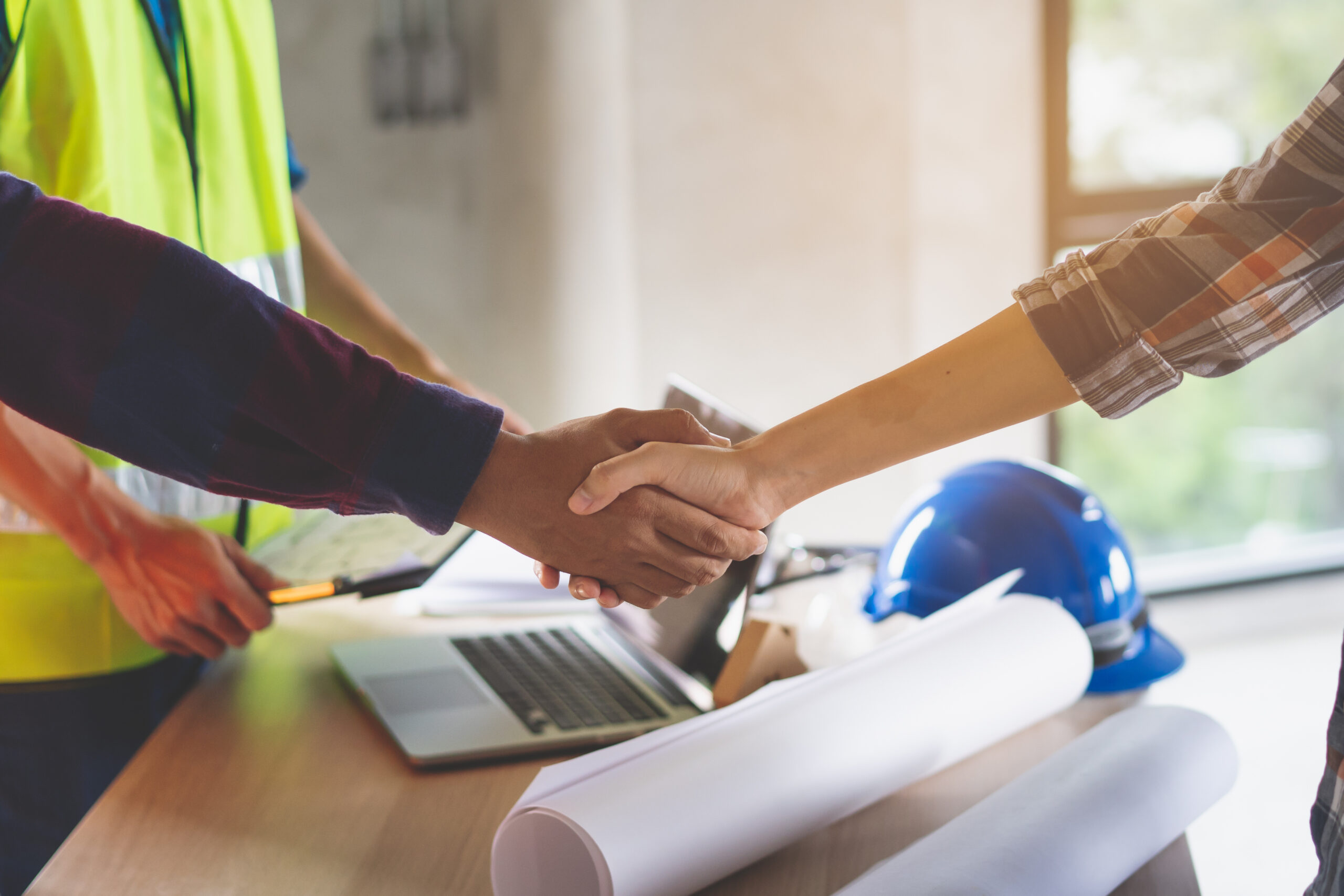 construction worker and contractor shaking hands over table and plans