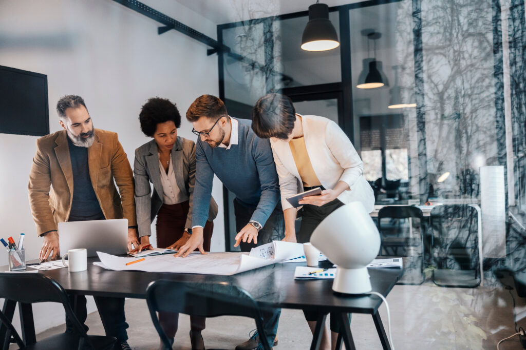 Team of business personnel is standing at a desk while looking at blueprints and plans